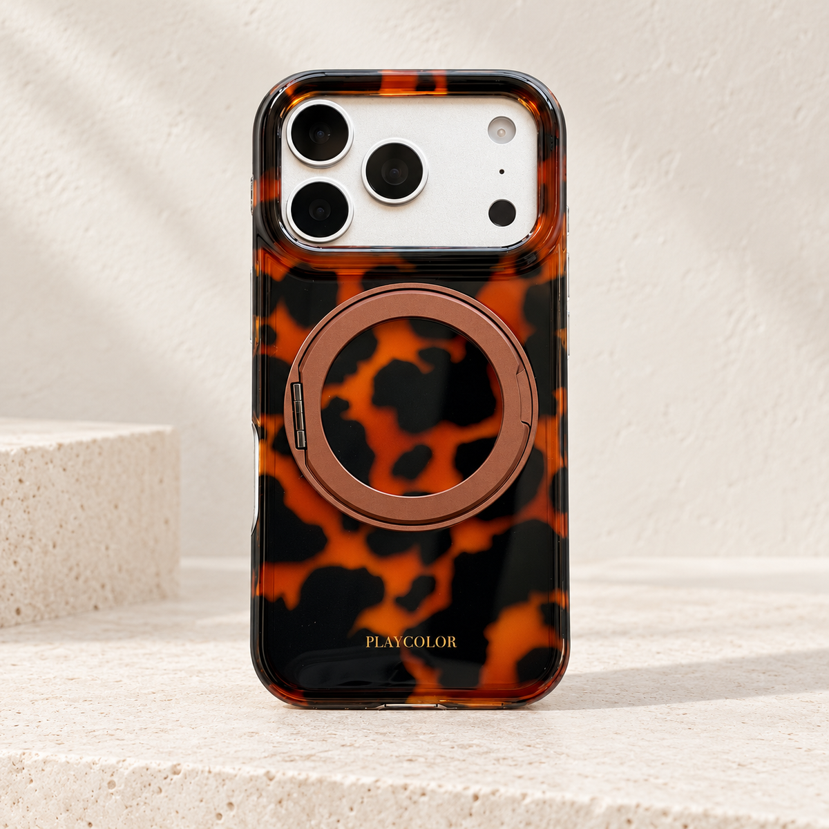 Amber tortoiseshell iPhone case with bronze-toned fold-out ring closed against the patterned back.