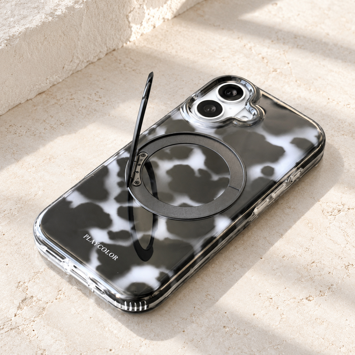 Grey tortoiseshell iPhone case lying diagonally with its hinged outer ring raised.