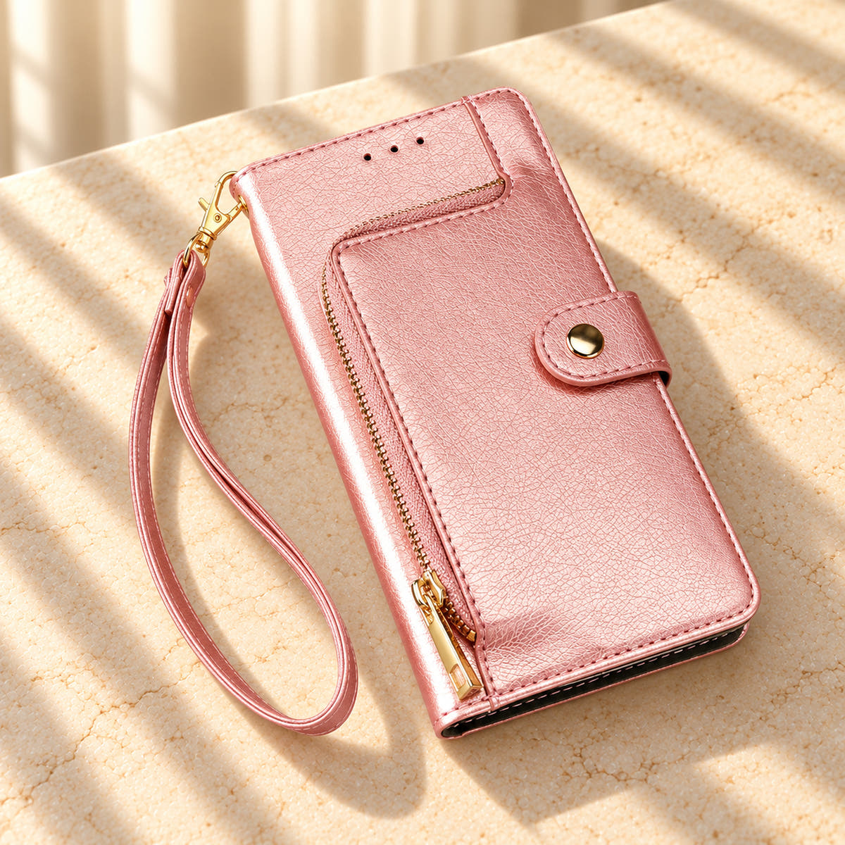 Valencia Luxe Pink wallet phone case on a cream stone tabletop with its curved zip pocket, round snap closure and matching wrist loop.
