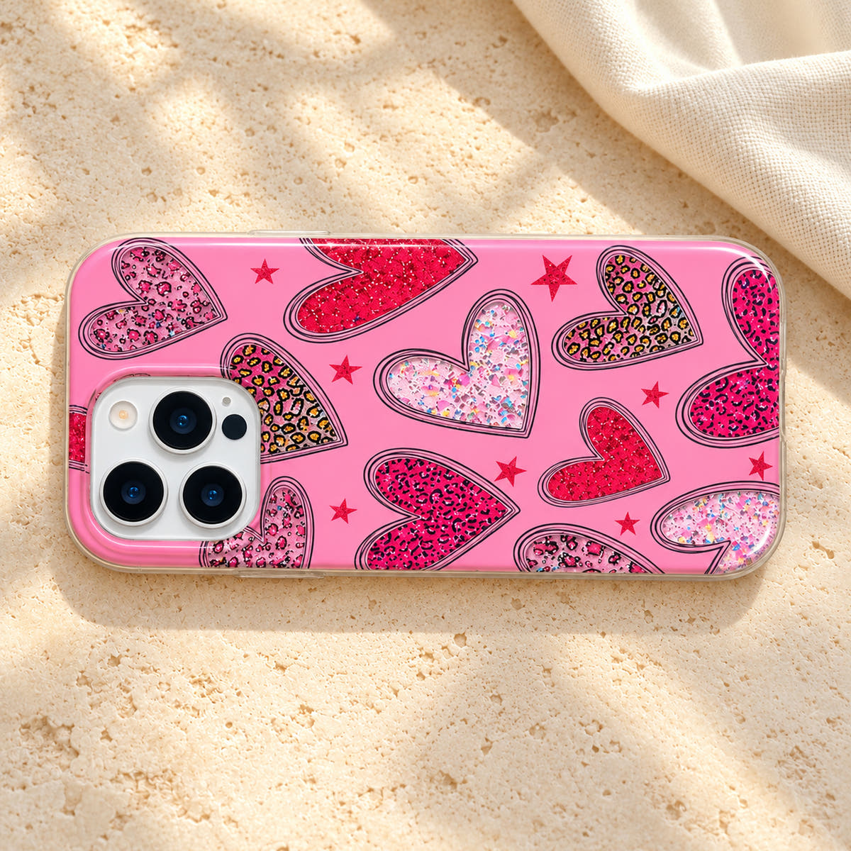 Horizontal flatlay of the Valentina Sparkle Heart Pink iPhone case on cream limestone with a small ivory linen accent.