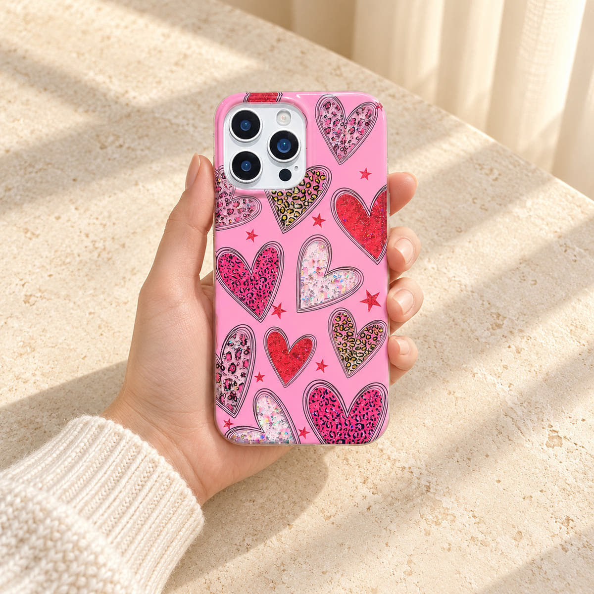 Wider in-hand view of the Valentina Sparkle Heart Pink iPhone case, showing the complete case against a cream-sleeved palm.