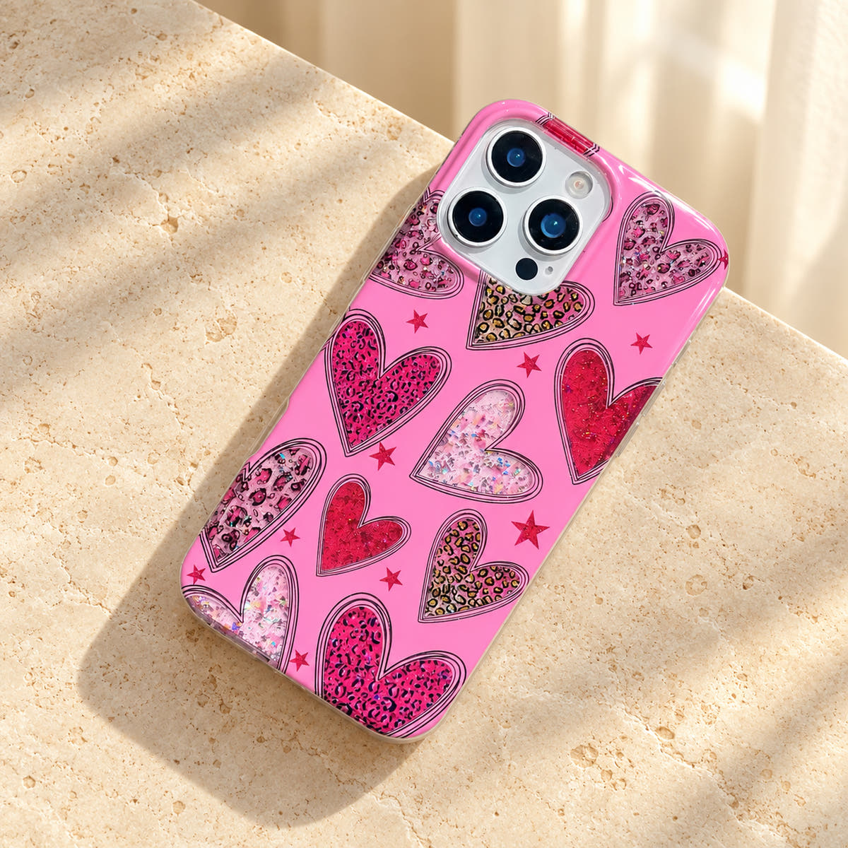 Valentina Sparkle Heart Pink iPhone case lying diagonally on a cream limestone tabletop, showing the full heart pattern.