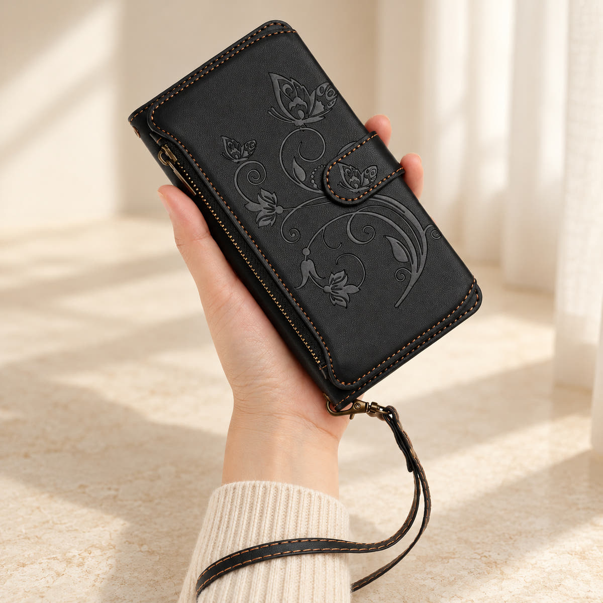 Velora Zip iPhone wallet case in Black, handheld with embossed butterfly front, side zip and matching wrist strap.